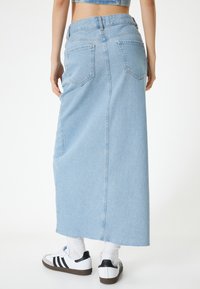 Vaaleansininen farkkukangas maksihame, jossa on istuva vyötärö ja kaksi takataskua. Helmassa on hieno hankauma. Yhdistettynä valkoisiin lenkkareihin ja sukkiin.