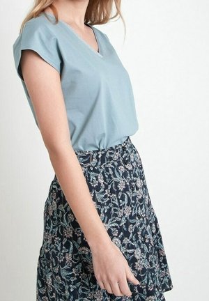 Femme portant un haut à manches courtes bleu clair avec un col en V, rentré dans une jupe taille haute bleu marine ornée de motifs floraux blancs et roses.