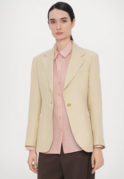 Beige textured blazer, single button closure, and two front pockets, layered over a light pink button-up shirt with long sleeves.