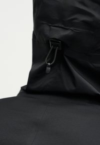 Melns jaku kapuce ar regulējamu elastīgo auklu un plastmasas aizbīdni pievilkšanai.