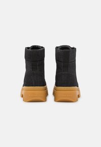 Bottines en denim noir avec une finition texturée et une semelle en caoutchouc brun robuste. Comprend une languette de tirage et des accents cousus.