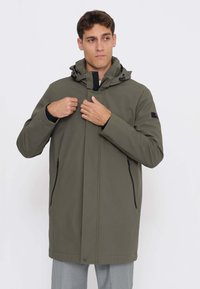 Giacca con cappuccio verde oliva con zip frontale, due tasche laterali e dettagli neri. Tessuto liscio, design di lunghezza media e cappuccio regolabile.