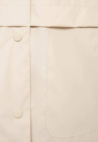 Beige regenjas stof met een soepele textuur, zijzak en knoopsluiting. Zichtbare stiksels langs de naden voegen detail toe aan het ontwerp.