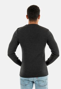 Maglione grigio scuro a maniche lunghe con un design attillato. Texture a coste sui polsini e sul colletto, indossato con jeans blu chiaro.