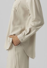 Hellbeige Langarmshirt aus weichem Stoff mit einer Brusttasche. Verfügt über einen lockeren Schnitt, abgerundeten Saum und geknöpfte Manschetten.