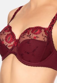 Reggiseno di pizzo borgogna con motivi floreali ricamati, pannelli trasparenti, spalline regolabili e bordi ondulati. Design strutturato con ferretto.