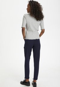 Grå ribbade kortärmade topp med scallopade kanter, matchad med marinblå byxor. Svarta skor fulländar outfiten och visar en elegant look.