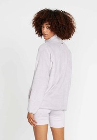 Giacca in pile viola chiaro con colletto alto, maniche lunghe e vestibilità rilassata, caratterizzata da una texture liscia e hardware minimal.