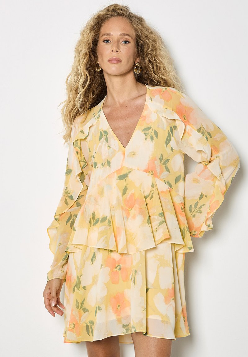 Robe jaune à motifs floraux avec un décolleté en V profond, des manches volantées et une jupe à volants superposés ; présente des accents pastel orange et vert, fabriquée en tissu léger.