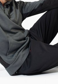 Pullover grigio bicolore con colletto alto e tasca frontale, abbinato a pantaloni neri, caratterizzati da texture lisce e linee di design eleganti.