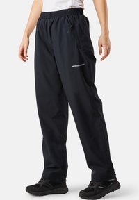 Person wearing black loose-fit outdoor pants with elastic waistband and zippered pocket, paired with black hiking shoes on white background.