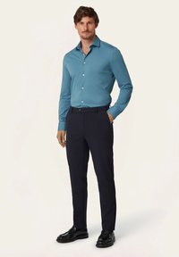 Herenoverhemd in lichtblauw met knopen, gecombineerd met donkerblauwe broek en zwarte instappers. Glad stof met lange mouwen en kraag.