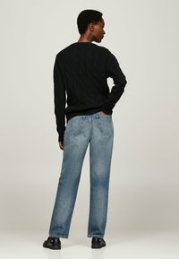 Pull en tricot noir à col rond, associé à un jean droit bleu clair et des chaussures noires, vu de dos.
