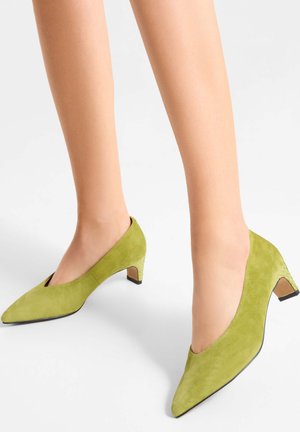 Green suede pumps with a low, angled heel. Features a pointed toe and a textured accent on the heel. Smooth finish, modern design.