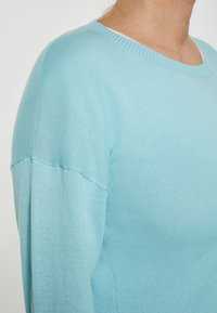 Jasnoniebieski sweter z okrągłym dekoltem i długimi rękawami. Miękka, gładka faktura z przeszyciami i żebrowanymi detalami wzdłuż dekoltu.