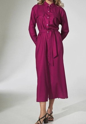 Mujer con vestido camisero midi de manga larga en color magenta con cinturón en la cintura, combinado con sandalias negras de tacón ancho con tiras.