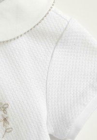 Indumento in cotone bianco con un motivo testurizzato, caratterizzato da un colletto rotondo decorato con piccole perle decorative e una sottile ricamo floreale.