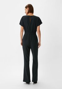 Czarny kombinezon z krótkimi, szerokimi rękawami, dopasowaną talią i rozszerzanymi nogawkami. Posiada detal w kształcie otworu na plecach oraz miękką, gładką teksturę.