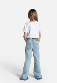 Biała koszulka z krótkim rękawem noszona z jasnoniebieskimi, wysokimi dżinsami, mającymi rozszerzany dół i małą brązową skórzaną metkę z tyłu.