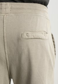 Beige Jogginghosen aus strukturiertem Stoff mit elastischem Bund und einer einzigen Gesäßtasche mit horizontaler Öffnung.