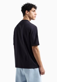 Maglietta nera a maniche corte con vestibilità rilassata, scollatura rotonda e texture liscia, abbinata a pantaloni blu chiaro.