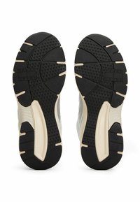 Suole di sneakers nere in gomma con motivi testurizzati e una suola intermedia bianca. Presenta un logo embossato nella zona del tallone e elementi di design curvi.