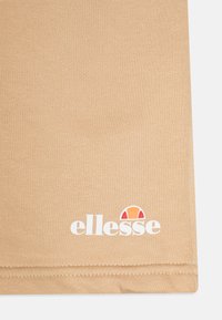 Bruna bomullsshorts har en ribbad struktur och en vit logotyp med en färgglad detalj, samt sömnadsdetaljer längs fållen.