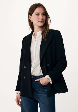 Černý dvouřadý blazer s klopami, s knoflíkovými detaily, nošený přes bílou strukturovanou košili a modré džíny. Hladký povrch látky.