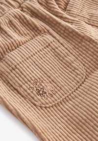 Brun kordfløjlstof med ribbet tekstur, der har en lomme og blomsterbroderi i subtile pink og brune nuancer.