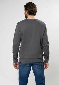 Grijze sweatshirt met lange mouwen en een ronde hals. De stof is glad met een losse pasvorm, gecombineerd met blauwe jeans met achterzakken.