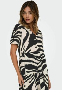 Robe à imprimé zèbre noir et crème avec des manches courtes, un col en V et des niveaux froncés, dotée d'une texture de tissu douce et fluide.