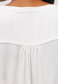 White blouse featuring a yoke design, gathered detailing at the back, and soft, textured fabric.