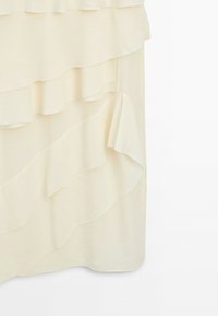 Tissu de couleur crème claire avec des volants superposés créant un motif fluide et texturé sur une jupe ou une robe douce.