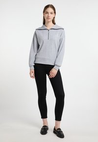 Szürke pulóver, cipzáros elülső résszel, széles gallérral és bordázott mandzsettával, fekete skinny farmerral és fekete loaferekkel párosítva. Puha pamut keverék anyag.