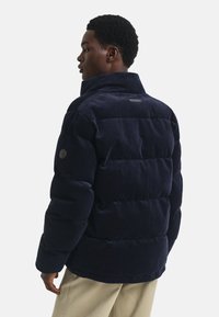 Marineblauwe corduroy puffer jacket met een hoge kraag, gestikte textuur en een zijlogo patch. Heeft een ontspannen pasvorm en een gladde afwerking.