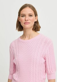 Rosa Strickpullover mit strukturierten Mustern und Kabelstrickakzenten, kurzen Ärmeln und Rundhalsausschnitt. Weicher Stoff mit gerippten Bündchen.