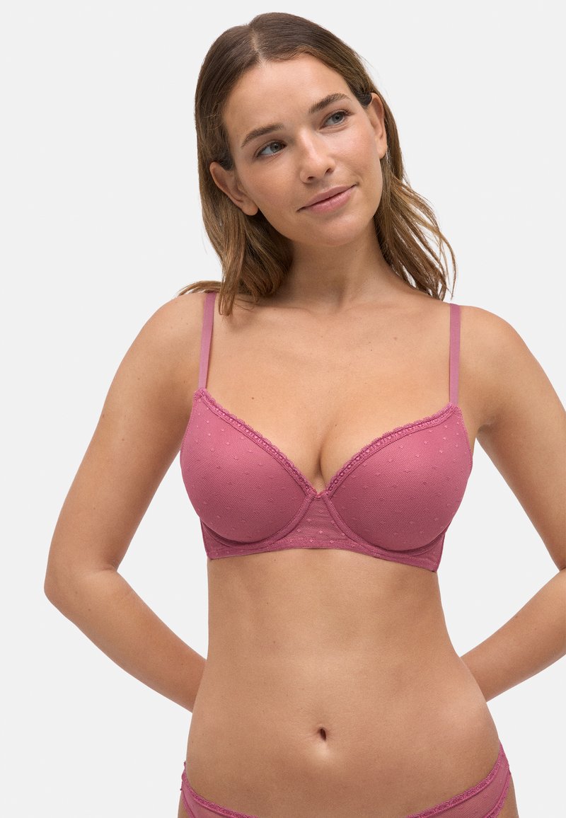 Sujetador rosa con textura de puntos, borde de encaje a lo largo de los bordes, tirantes ajustables y un diseño estructurado y de soporte.