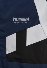 Tkanina sportowa w kolorze granatowym, czarnym i białym z logo "hummel SPORTSWEAR" nadrukowanym jasnoszarym kolorem na granatowym fragmencie.