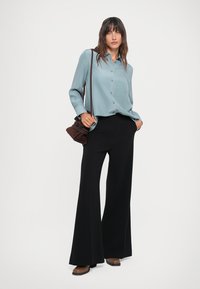 Light blue button-up shirt, black wide-leg trousers, and brown flats. The outfit features a casual style, complemented by a brown shoulder bag.