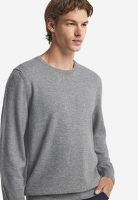 Grauer Pullover aus weichem Stoff, mit Rundhalsausschnitt, langen Ärmeln und entspannter Passform. Mit gerippten Bündchen und Saumdetails.