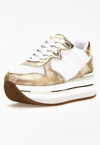 Baskets dorées et blanches avec une finition métallique brillante, un motif graphique, des lacets blancs, une languette rembourrée, et une semelle blanche épaisse avec une bande de roulement marron.