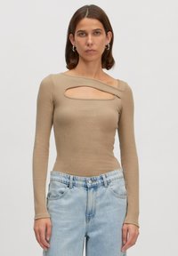 Beige top met lange mouwen en ribbeltextuur, heeft een unieke hoekige uitsnede over de borst, gecombineerd met lichtblauwe hoge taillejeans.