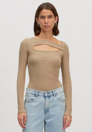 Langärmliges beiges Oberteil mit gerippter Textur, verfügt über einen einzigartigen schrägen Ausschnitt über der Brust, kombiniert mit hellblauen hochtaillierten Jeans.