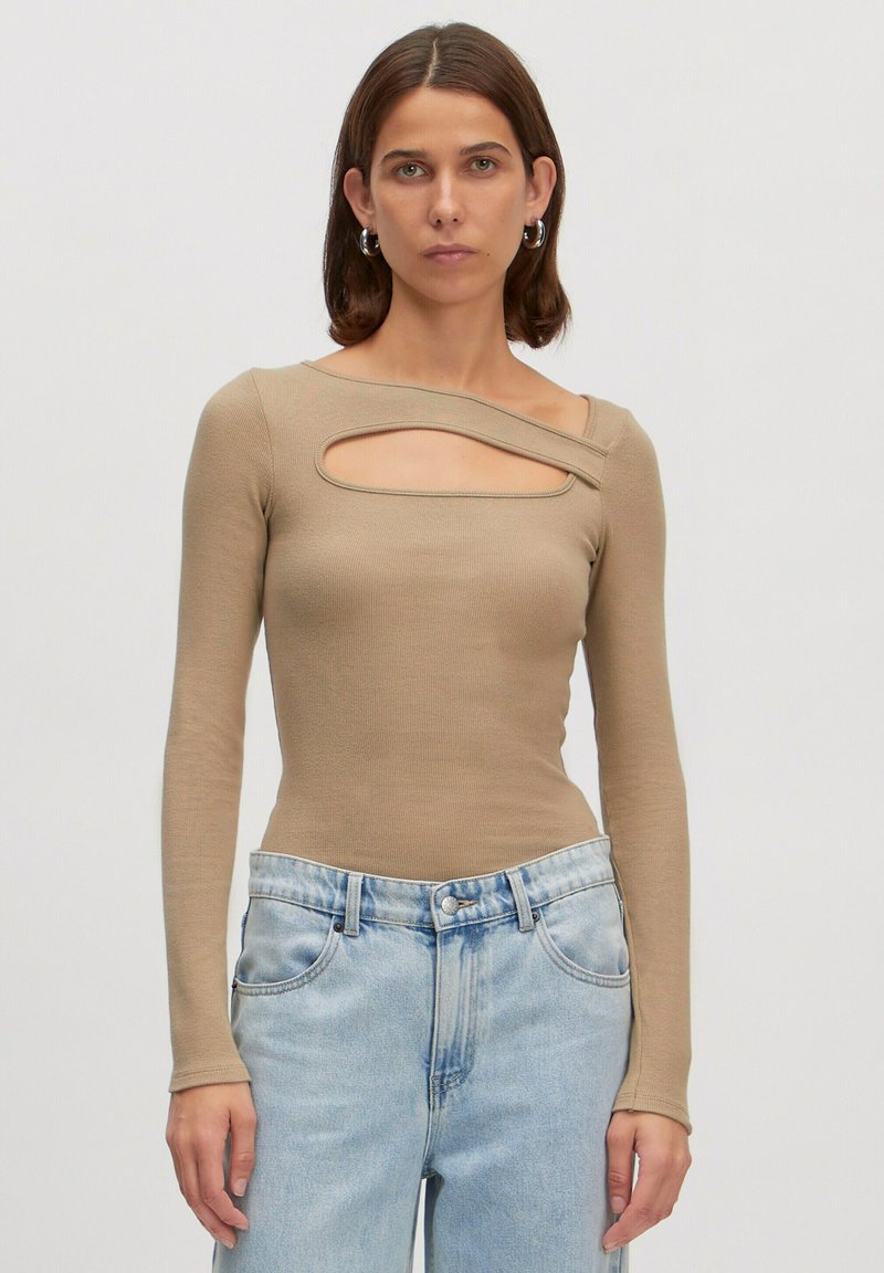 Beige top met lange mouwen en ribbeltextuur, heeft een unieke hoekige uitsnede over de borst, gecombineerd met lichtblauwe hoge taillejeans.