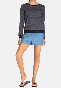 Camiseta negra de manga larga con un patrón texturizado, combinada con pantalones cortos de mezclilla azul claros. El modelo lleva chanclas negras.