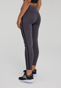 Legginsy w wysokim stanie, dopasowane, w ciemnoszarym kolorze z czarnymi paskami po bokach. Wykonane z elastycznego materiału o gładkiej teksturze. Połączone z czarnymi butami.