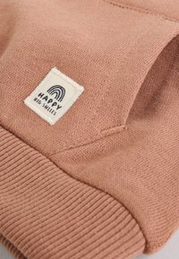 Hele roosa dressipluus soonikkoes varrukate ja äärega, millel on ruudukujuline logomärk tekstiga "HAPPY BIG SMILES" ja vikerkaare kujundusega.