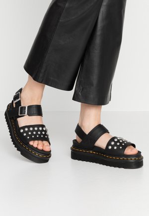 Sandales à plateforme noires en cuir, avec des clous argentés sur la bride avant, des boucles réglables et des semelles en caoutchouc texturé avec un accent jaune.