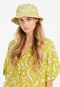 Groene bucket hat met een wit bladenpatroon, gemaakt van stof. Beschikt over een brede rand en een logo-patch aan de voorkant. Casual ontwerp, ongestructureerde vorm.