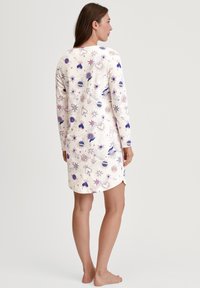 Vestito da notte a maniche lunghe in tessuto morbido, con base crema e fantasie colorate di cuori, stelle e oggetti celesti, caratterizzato da un orlo leggermente curvo.